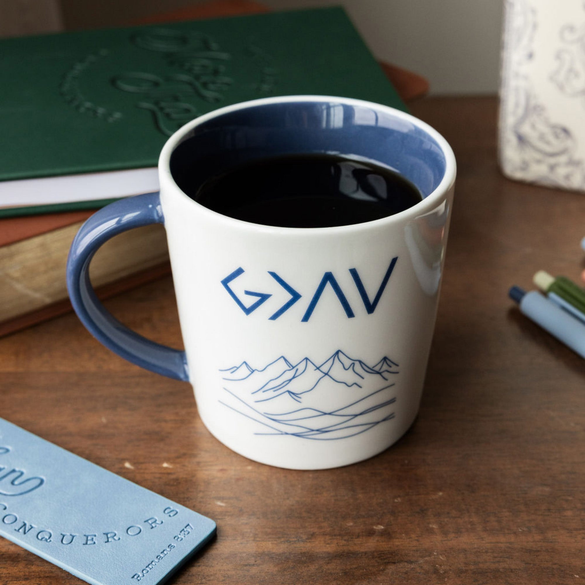 White mug with blue interior and handle, featuring 'G>AV' text and mountain design on a white background on a desk