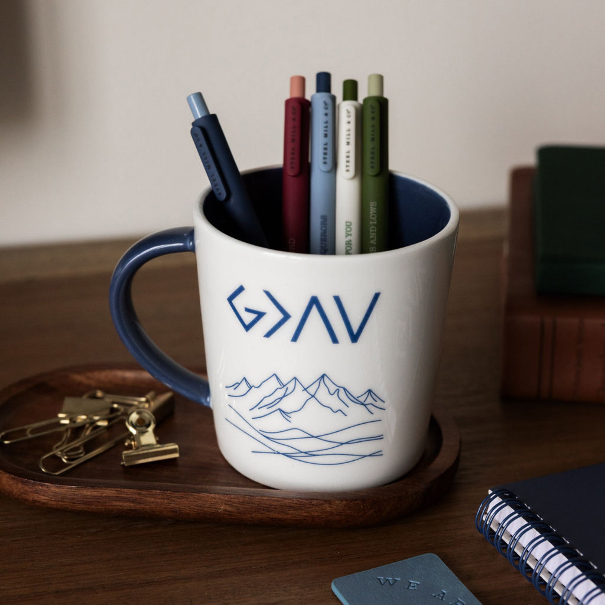 White mug with blue interior and handle, featuring 'G>AV' text and mountain design on a white background with pens inside